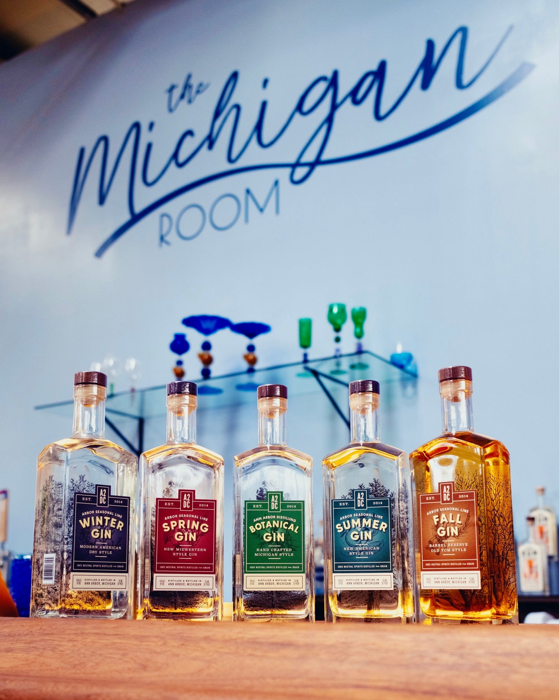 Row of gin bottles on a wooden surface with 'The Michigan Room' sign in the background