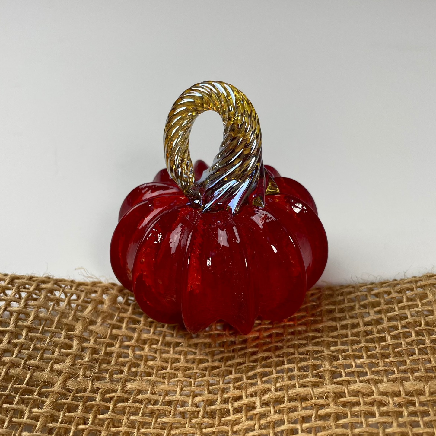 Red glass pumpkin with gold stem on a textured brown surface