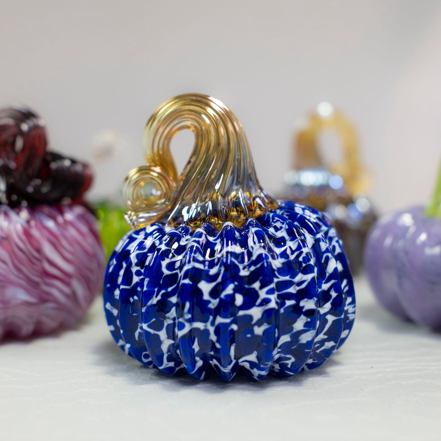 A spotted white and blue mini pumpkin sits in front of a white background.