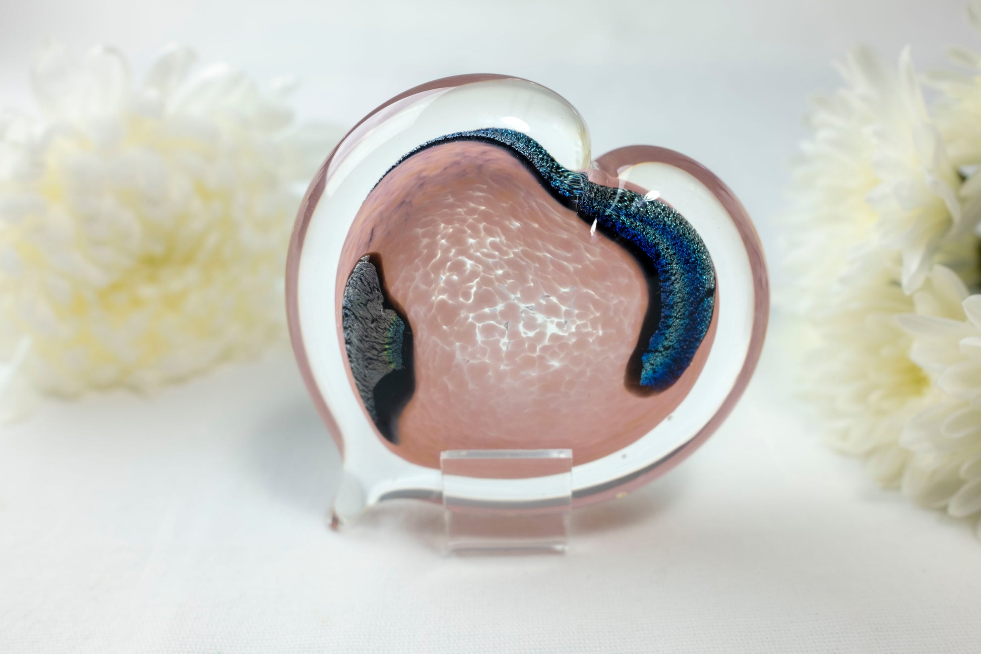 A light pink heart with chromatic swirls sits in front of white flowers.