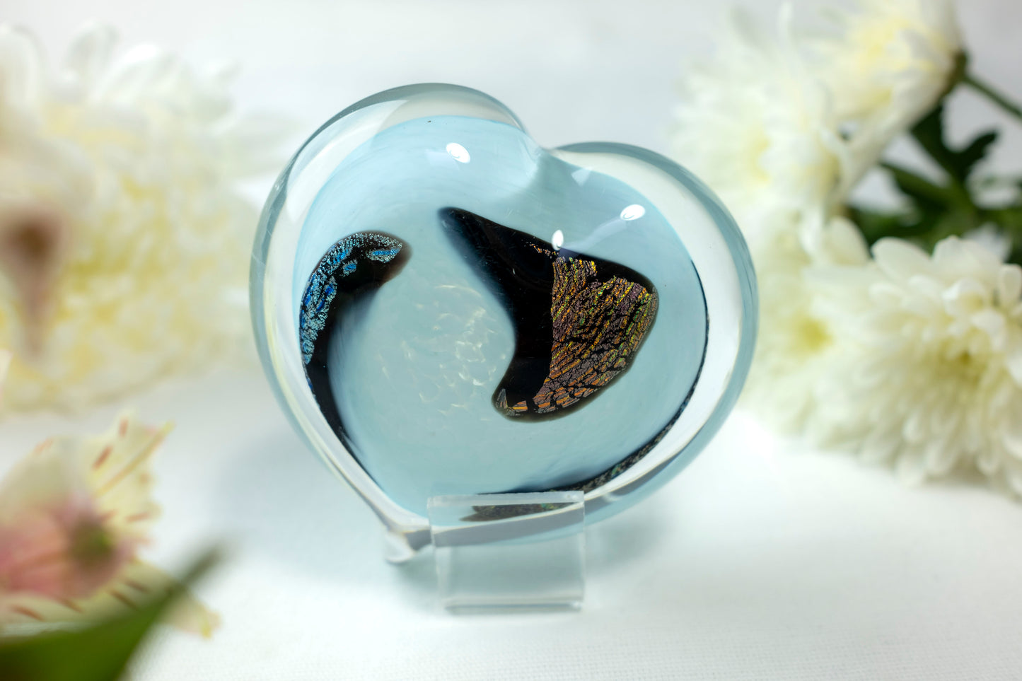 A baby blue heart with chromatic swirls sits in front of white flowers.