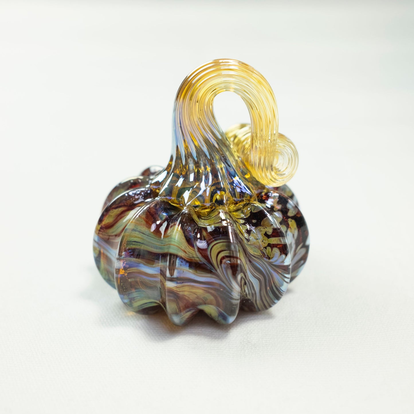 A green and brown swirled mini pumpkin sits in front of a white background.