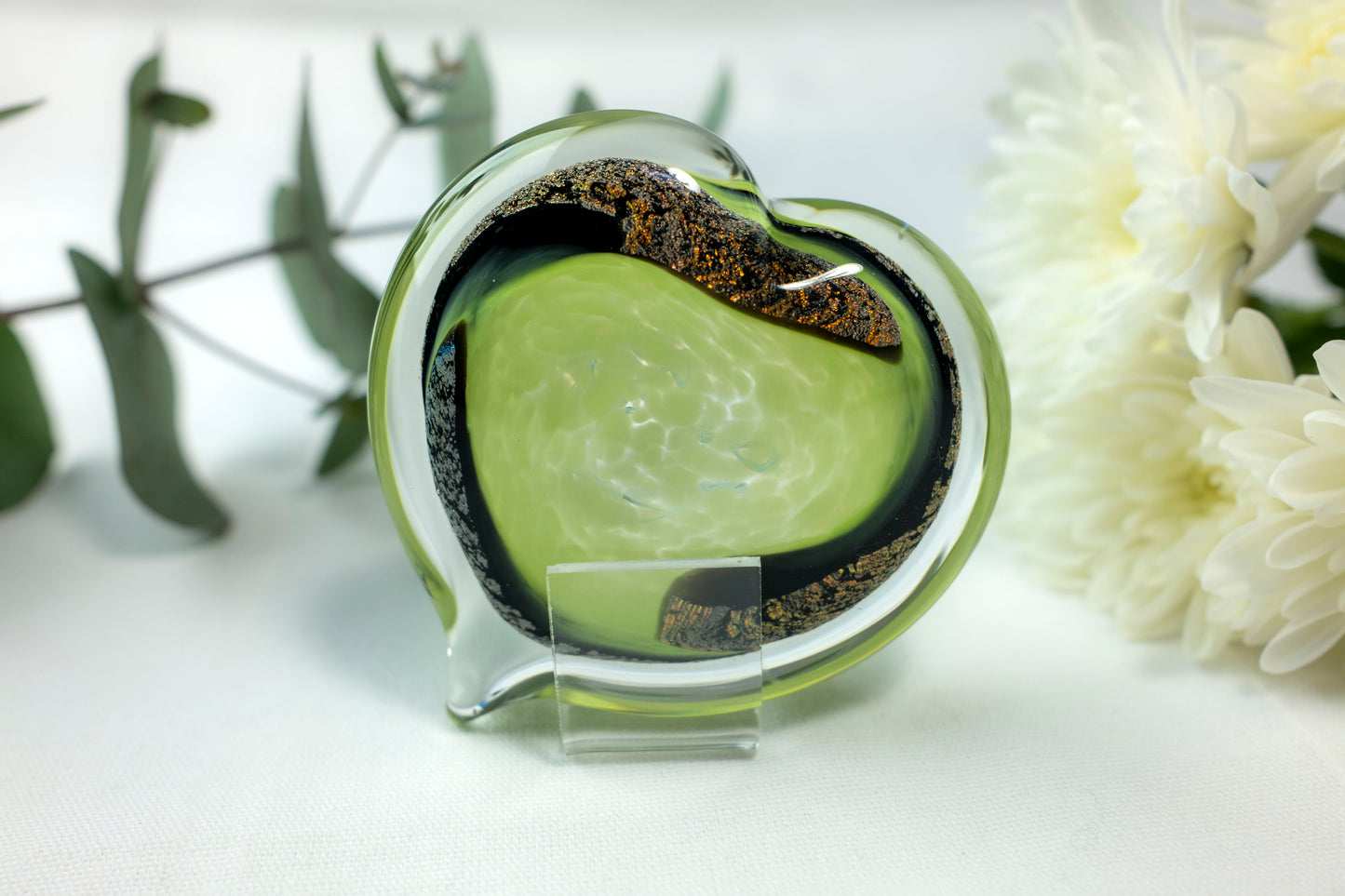 A lime green heart with chromatic swirls sits in front of white flowers.