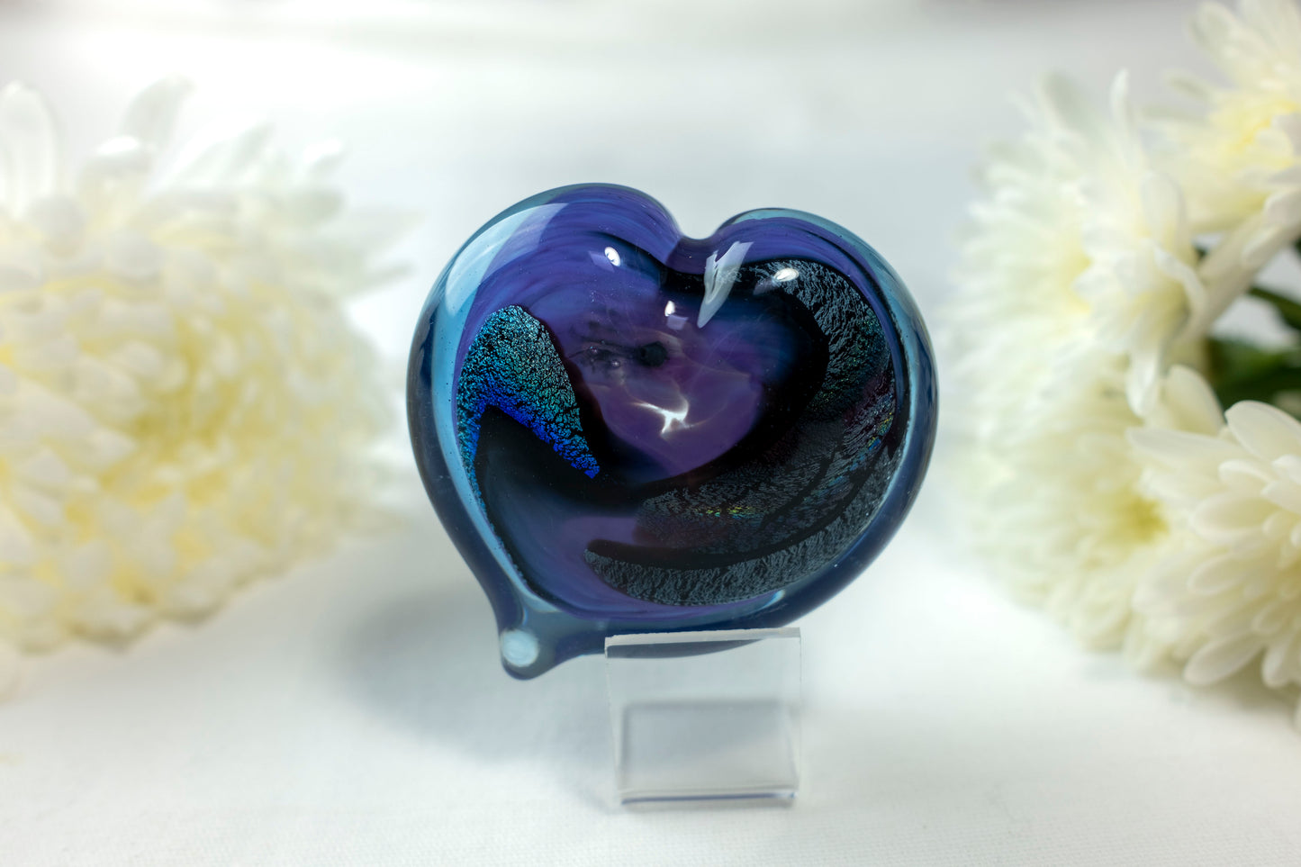 A purple and blue heart with chromatic swirls sits in front of white flowers.