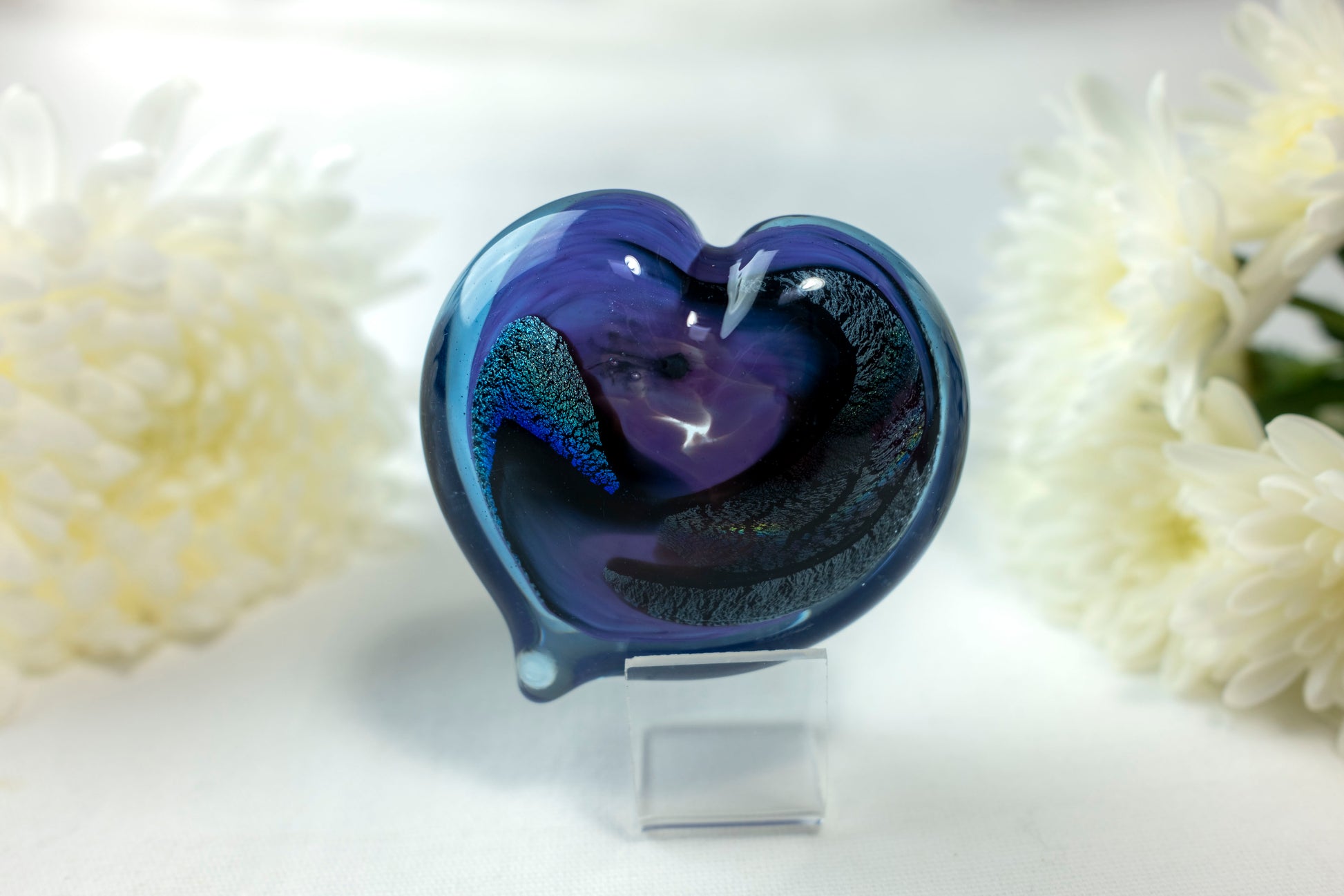 A purple and blue heart with chromatic swirls sits in front of white flowers.