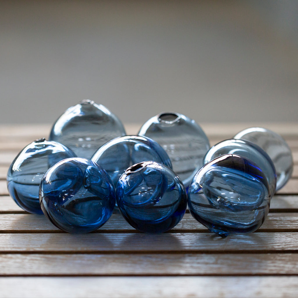 Nine Breath of Michigan Bubbles of varying shades of blue lay on a wooden surface.