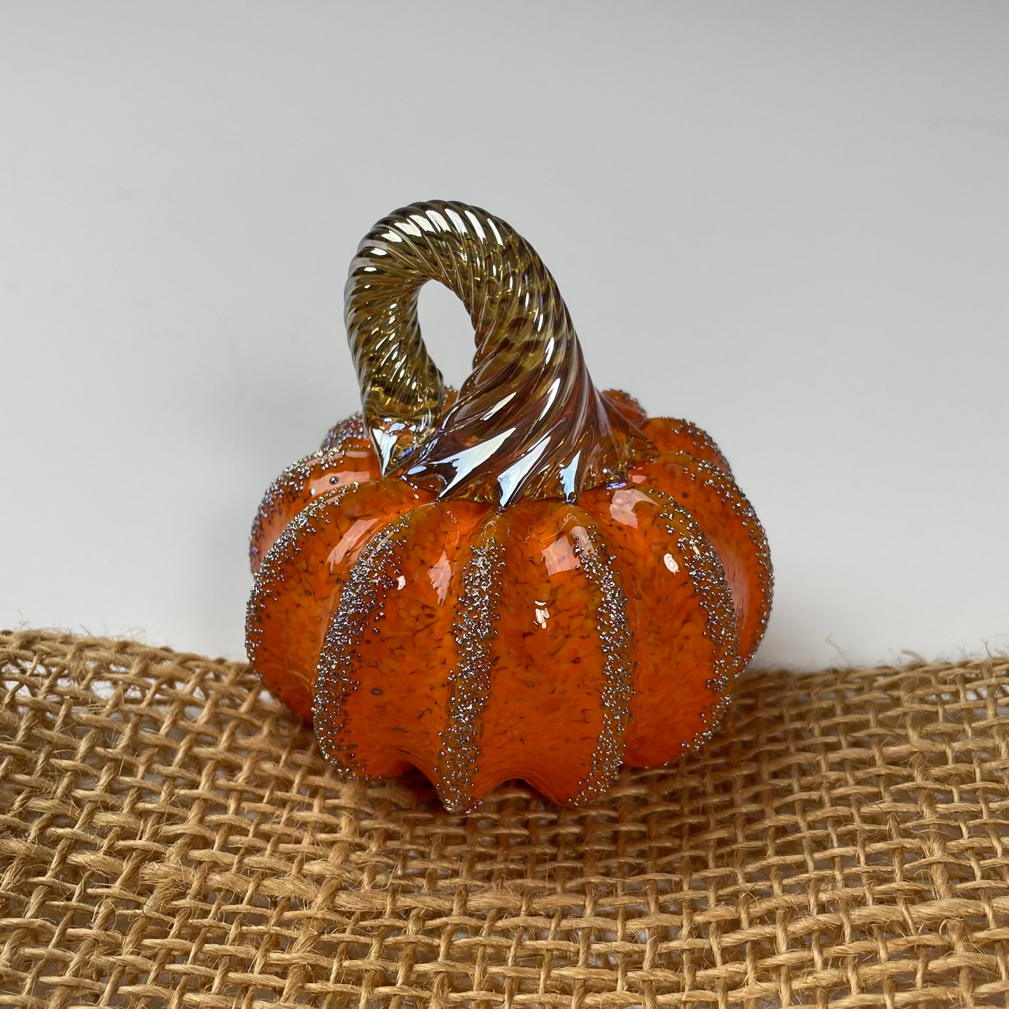 Decorative orange and gold glass pumpkin on a burlap surface