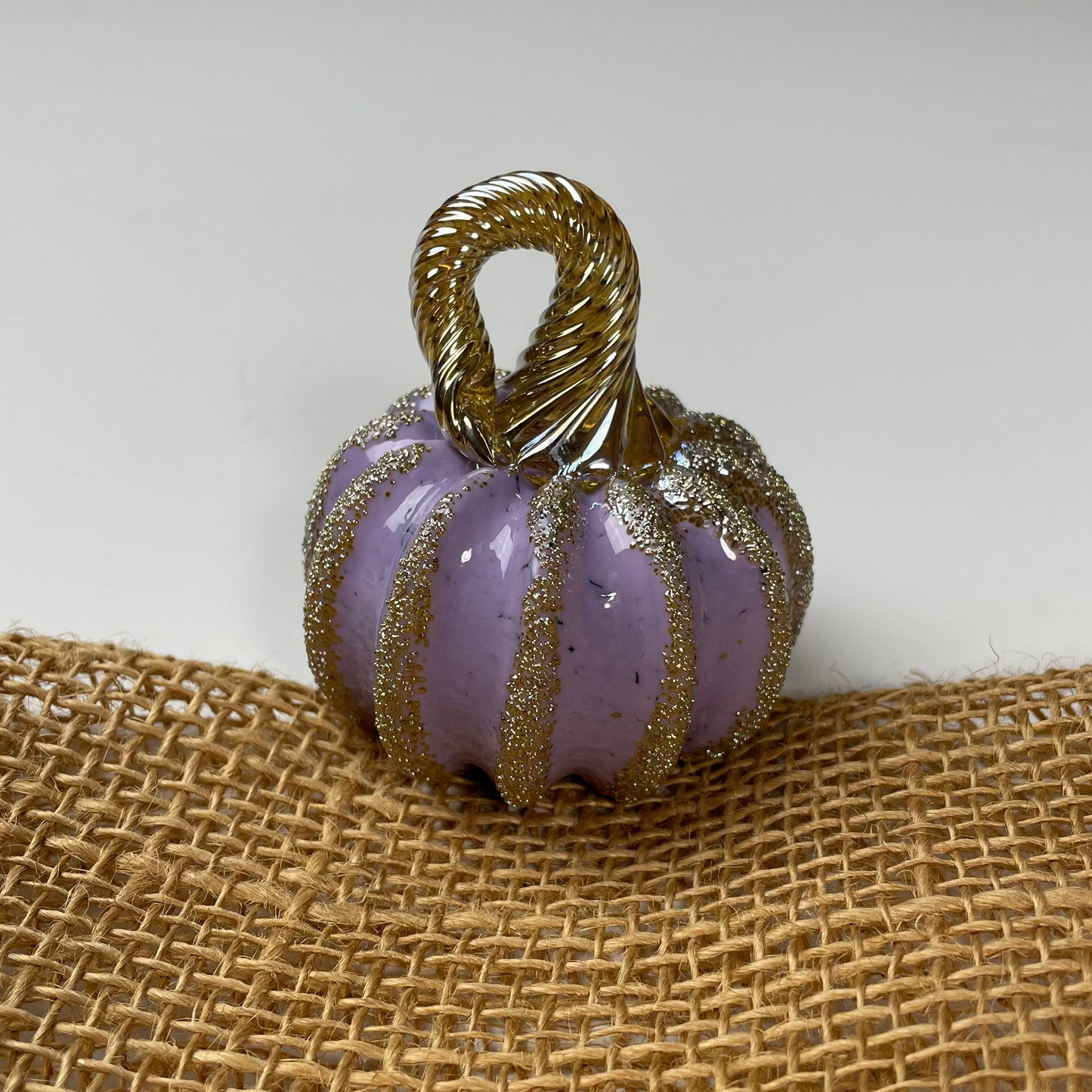 Decorative purple pumpkin with gold accents on a burlap surface