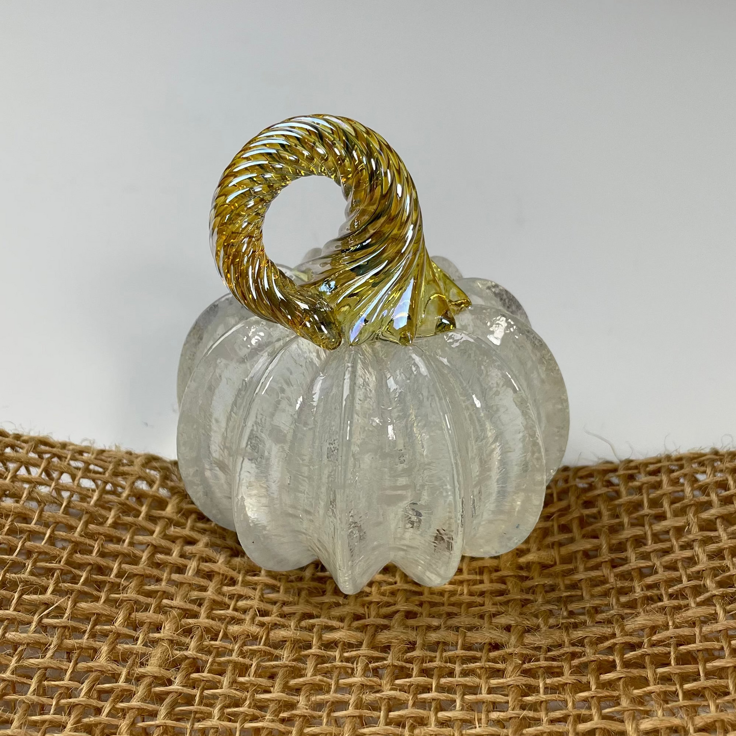 Clear glass pumpkin with gold stem on a burlap surface