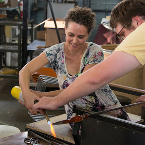 A student at the Glass Academy and glass blowing instructor work together to create a glass sculpture