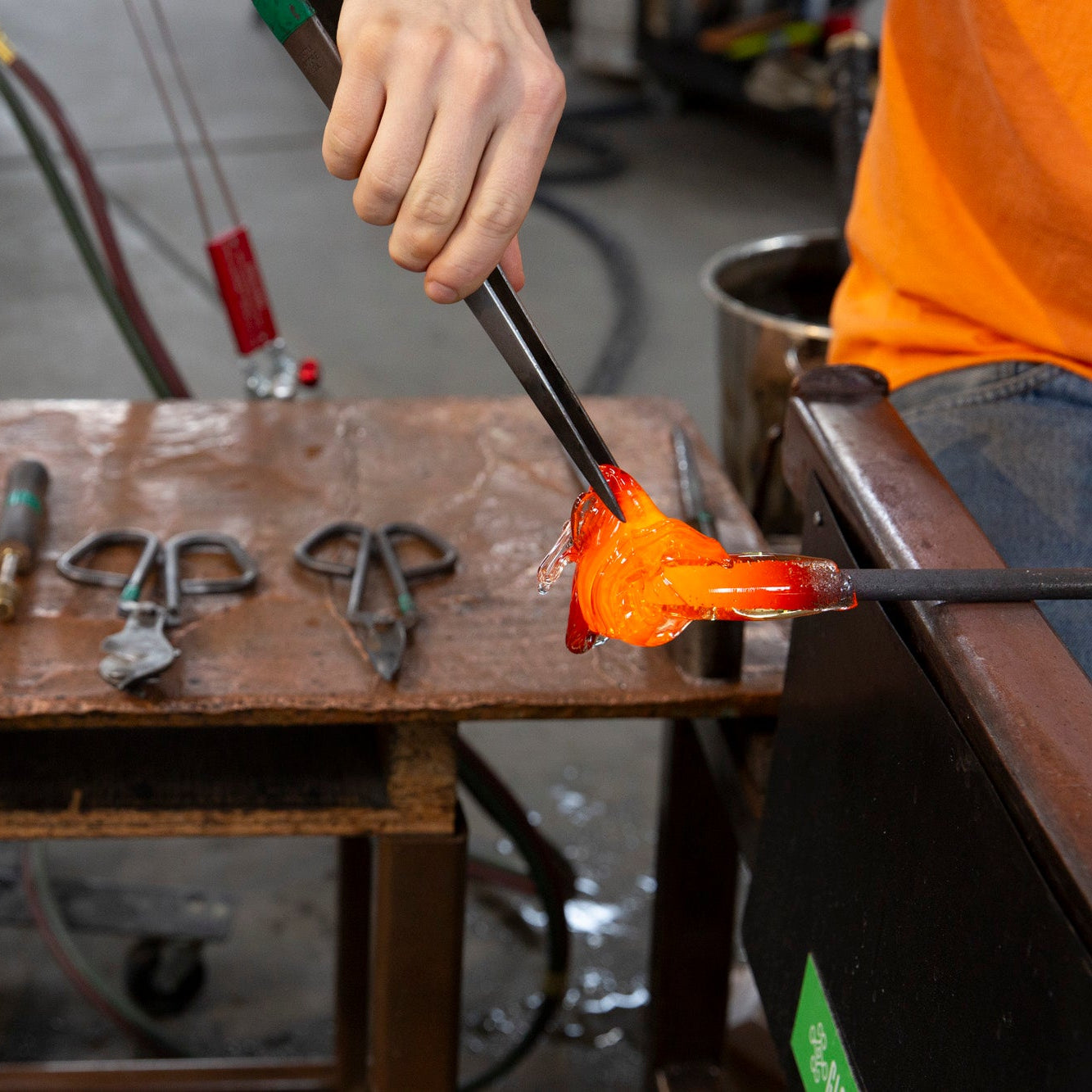 A 100% Hands-On class student works with large tweezers to pull a gather of molten glass.