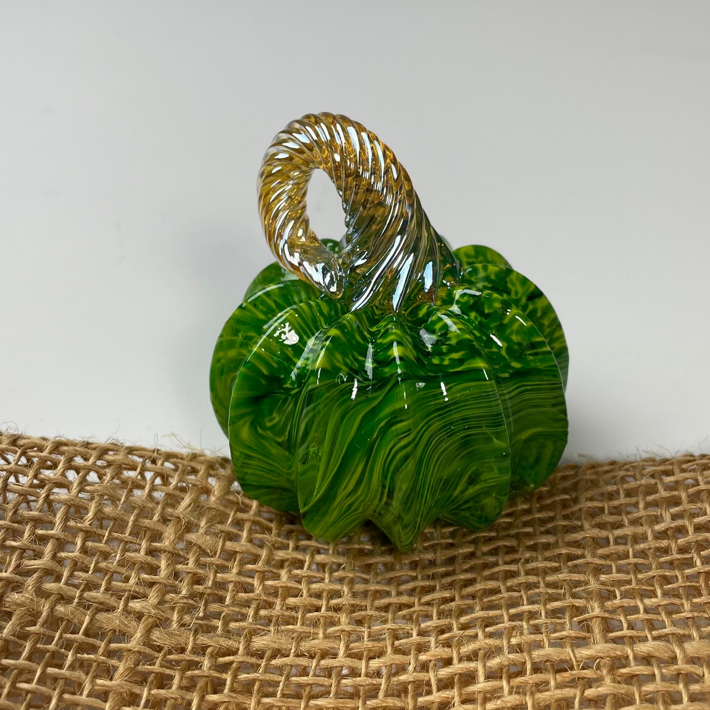 Green glass pumpkin with gold stem on a textured brown surface