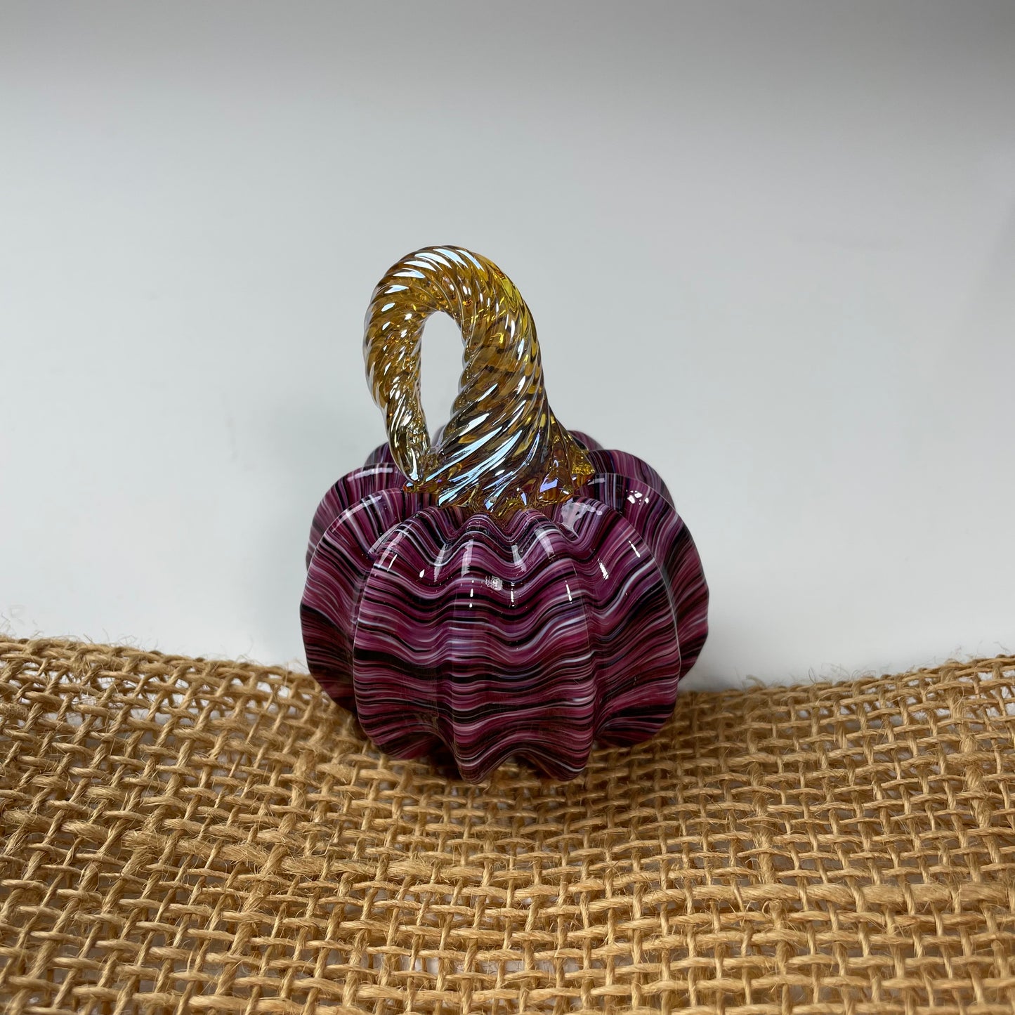 Decorative glass pumpkin with purple wavy design on a textured surface