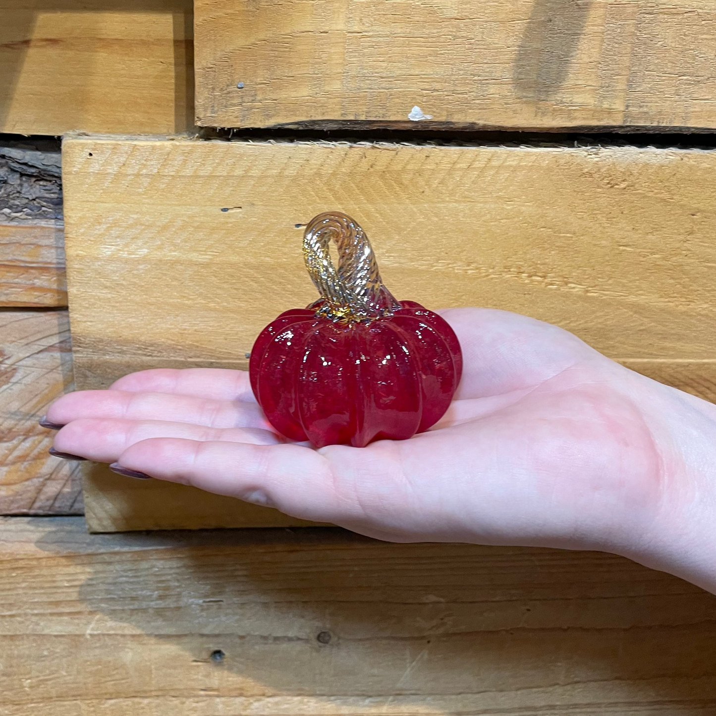 Small red glass pumpkin held in a hand against a wooden background
