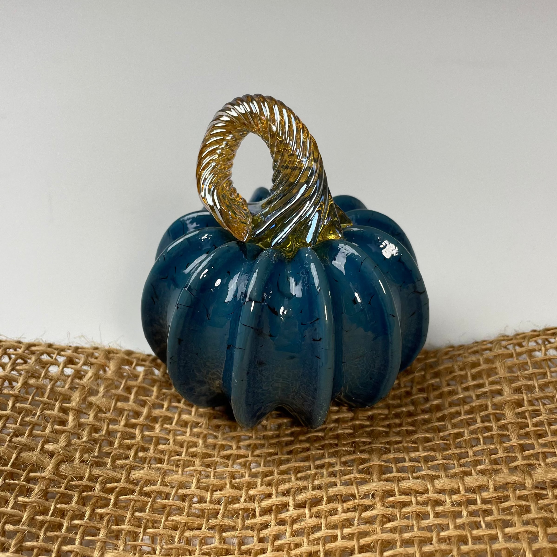 Blue glass pumpkin with a gold stem on a burlap surface