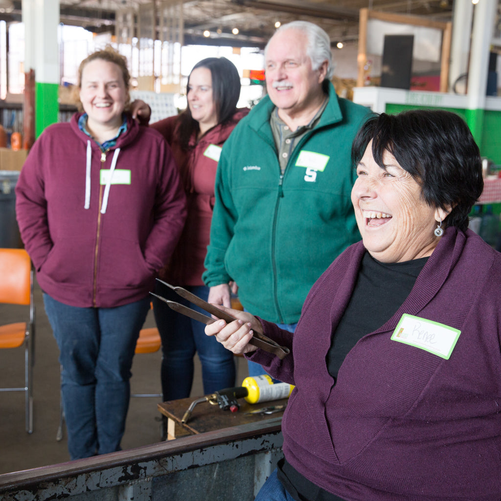 Breath of Michigan class students laugh as their glassblower gives them a safety demonstration.