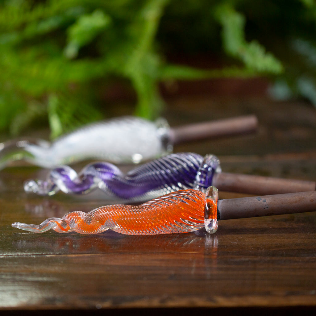Orange, a purple, and a white Percolla Reed garden sculptures on a table  